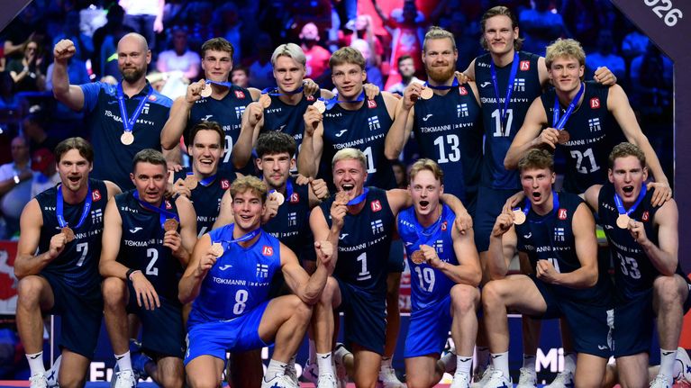 Suomen miesten lentopallomaajoukkue poseeraa ryhmäkuvassa mitalit kaulassa.