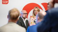 En man och en kvinna står framför en vägg med SDP:s logotyp.