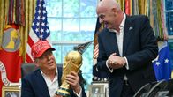 En man med röd keps med texten "MAKE AMERICA GREAT AGAIN" håller i en VM-pokal tillsammans med en kostymklädd man i ett kontor.