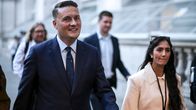 Wes Streeting kävelee tummassa puvussa kadulla seurassaan muita ihmisiä, taustalla kivirakennus.