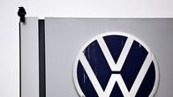 Suurikokoinen Volkswagenin logo harmaan rakennuksen seinässä. Vieressä istuu musta lintu.