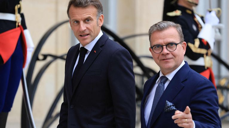 Emmanuel Macron and Petteri Orpo walking into a building with two military guards behind them.