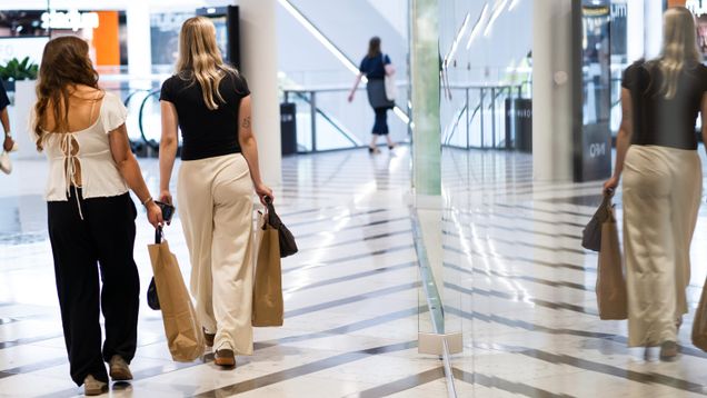 Two young women walk through a shopping centre carrying shopping bags.