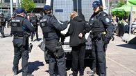 Några poliser står med en gripen person bakom en polisbil.