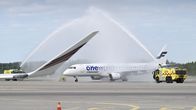 A white passenger jet receiving a water salute from two yellow fire trucks on an airport runway.