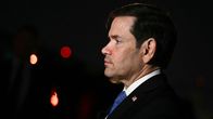 Marco Rubio seisoo sivuprofiilissa pimeässä valaistulla alueella, päällään hänellä on puvuntakki ja sininen solmio, taustalla valopisteitä.