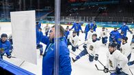 Jääkiekkovalmentaja piirtää kuviota taululle mieskiekkoilijoiden kuunnellessa kaukalossa.