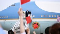 Donald Trump seisoo Air Force One -lentokoneen oviaukolla. Joukko ihmisiä heiluttaa pieniä Kiinan lippuja lentokoneen vieressä.
