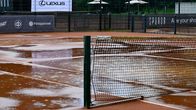 Sateen kastelema tenniskenttä, jonka verkko on osittain kaatunut; taustalla mainoskylttejä, mm. "Lexus".