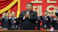 Kim Jong-Un puku päällään, taustalla joukko miehiä taputtavat käsillään.