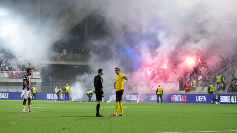 Petteri Pennane juttelee tuomareille, kun taustalla Trabzonsporin fanit ampuvat ilotulitteita.