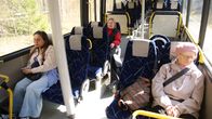 Bussin sisätiloissa paistaa aurinko ja kolme ihmistä istuu penkeillä.
