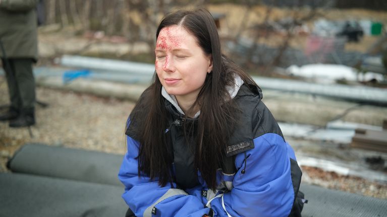 Isa Tarvainen sinisessä kelkkahaalarissa ulkona, tekoveriroiskeita naamassa.