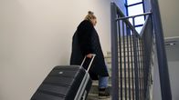 Nainen nousee kävellen portaita, perässään vedettävä matkalaukku.