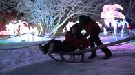 Talvisessa valopuistossa kaksi henkilöä joista toinen istuu napakelkassa ja toinen työntää.