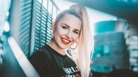 Laulaja Ilta katsoo hymyillen suoraan kameraan nojaten metalliseen aitaan. Kuva rajattu rintakehästä alaspäin.