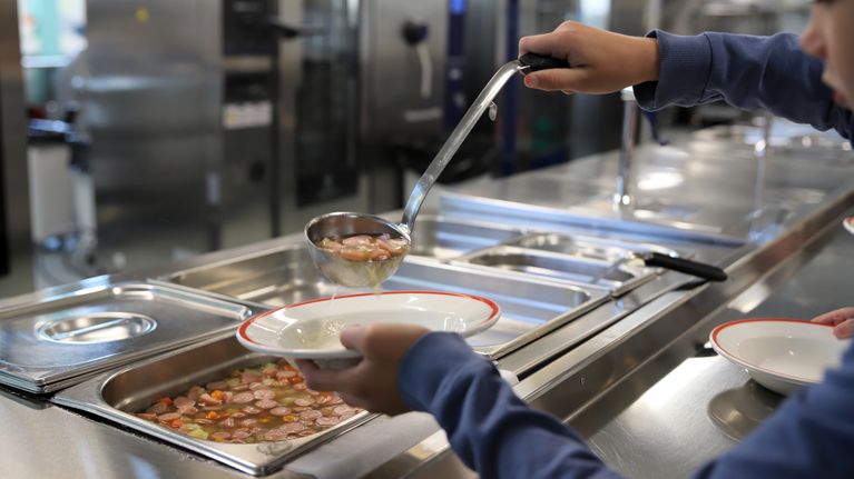 Lapsi annostelee nakkikeittoa koulun ruokalassa. 