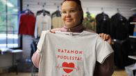 Henkilö pitää käsissään vaaleaa t-paitaa, jossa lukee punaisella "RATAMON PUOLESTA! 2026" ja sydänkuvio. Taustalla vaaterekkejä.