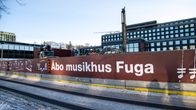 Ett staket runt ett bygge, Åbo musikhus Fuga står på staketet.