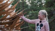 Nellie Wallden koskettaa suurta, puusta tehtyä taideteosta, jossa on liikkuvia siipimäisiä ulokkeita.