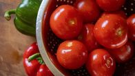 Tomaatteja metallisessa lävikössä, puisella leikkuulaudalla punainen ja vihreä paprika.