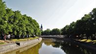 Aura Å mitt i sommaren. På bilden syns grönskande träd, biblioteksbron och domkyrkan i bakgrunden. Fotot är taget från Aurabron. 