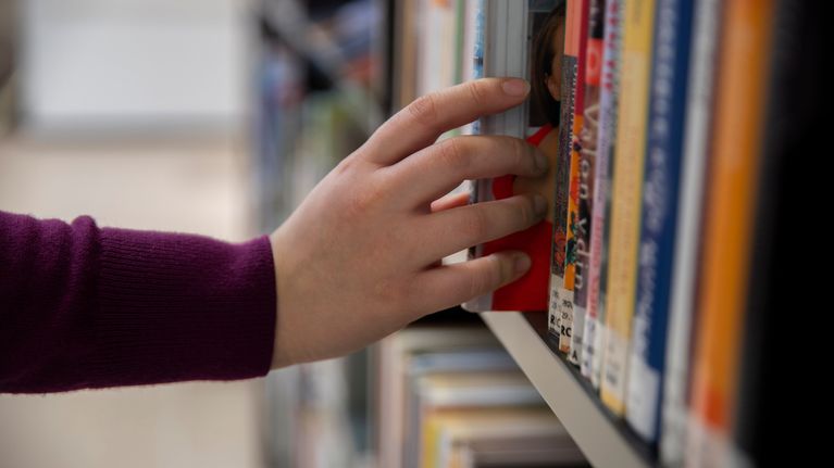 Jenni Kaukoranta ottamassa kirjaa kirjahyllystä Kotkan kaupunginkirjastolla.