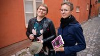 Tutkija Elina Karvo ja Suvi Laine poseeraavat Sherlock Holmesin hatun ja kirjojen kanssa Vanhan Suurtorin maisemassa.