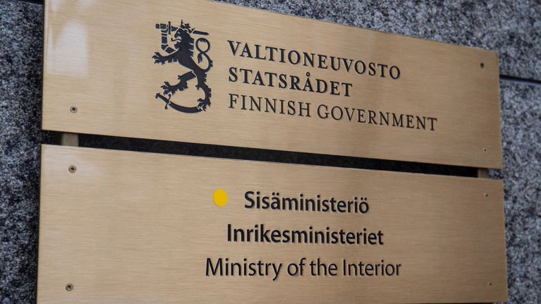 Gold coloured sign on a granite wall, reading "Ministry of the Interior" in Finnish, Swedish and English in black lettering.