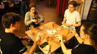 Fyra unga personer spelar kort tillsammans vid ett bord med drycker.