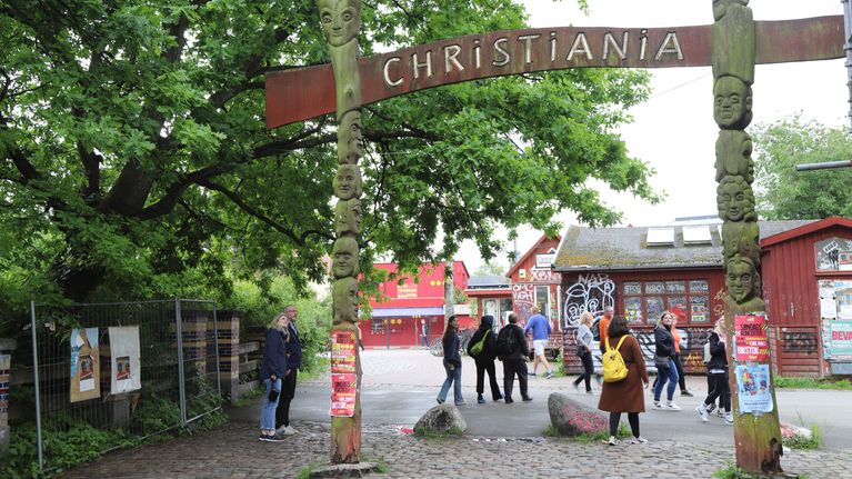 Christianianin portti. Puisiin paaluihin on kaiverrettu naiveja kasvoja, kahden paalun välillä kyltissä lukee Christiania.