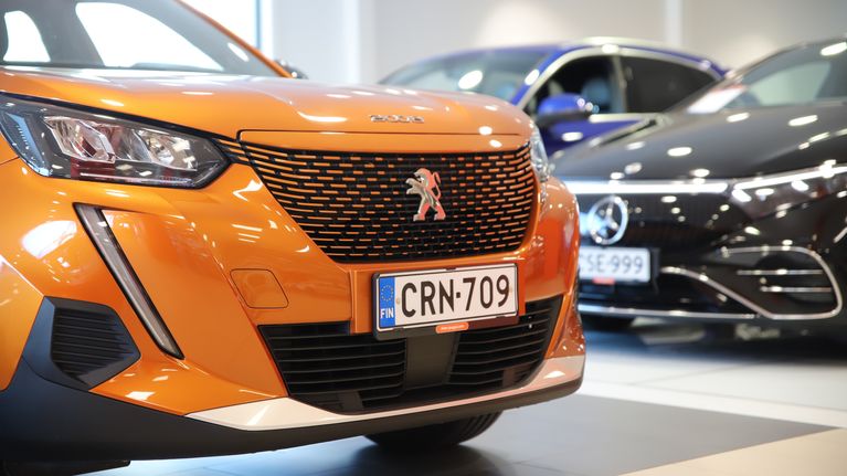Oranssi Peugeot ja musta Mercedes-benz seisovat vierekkäin autoliikkeen sisätiloissa.