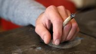 Mies leputtaa kättää pöydän päällä. Kädessä on kannabissätkä.
