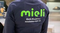 A person seen from behind wearing a dark colored shirt with the word Mieli on it in green stylised lettering.