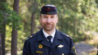 Pelastaja työasussaan katsoo kameraan. Taustalla metsää. 