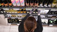 Myyjä asettelee viinipulloja Alkon hyllylle Kuopion Savilahden Alkossa. 