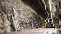 A worker in a yellow hi-vis outfit with cables and machinery in a tunnel deep underground.