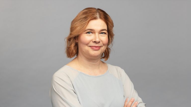 Minna Mustakallio yllään vaalea paita ja käsivarret ristissä