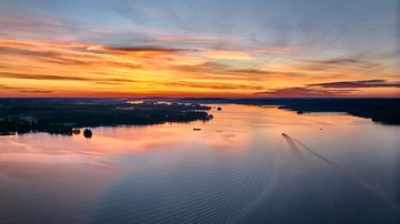 Kesäillan taikaa Sastamalassa.Ilmakuva järveltä, jossa vene seilaa kohti auringonlaskua. 