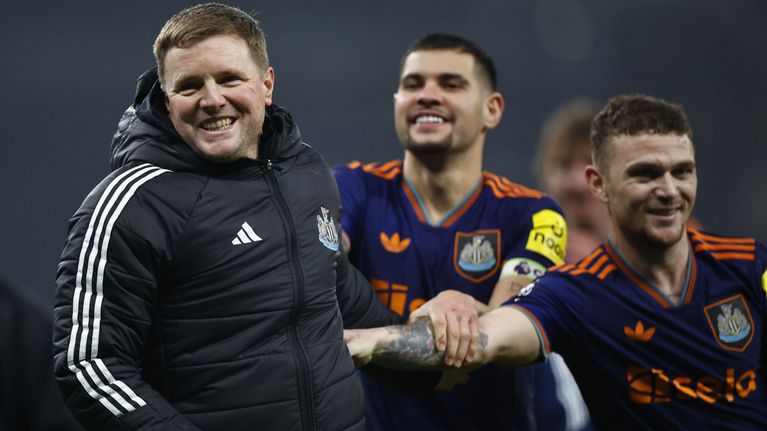 Tre personer i Newcastle United-kläder står tillsammans på en fotbollsplan; två bär matchtröjor med Adidas-logotypen.