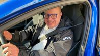 Autoliiton koulutuspäällikkö Teppo Vesalainen istuu sinisen henkilöauton ratissa ja hymyilee.