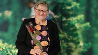 EN kvinna står med en ros i handen.