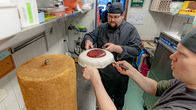 Two bakers lifting the icing on to an oversized Runeberg pastry.