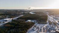 Ilmakuva kevyesti lumipeitteisestä maisemasta, jossa on metsää sekä teollisuus- ja yritysalueita tavoitteeseen. Etualalla näkyy pysäköintialue ja rakennuksia, ja horisontissa erottuu tehtaan piippujen savua.