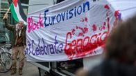 Mielenosoittaja heiluttaa Palesatiinan lippua. Pakettiauton kyljessä on lakana, jossa lukee "block eurovision, don't celebrate genocide"