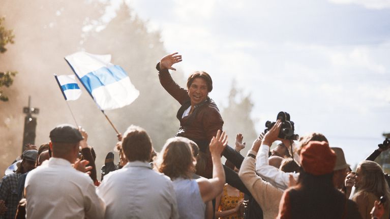 Ihmisjoukko nostaa ilmaan Jarno Saarista (Tom Rejström), joka tuulettaa riemukkaasti kameralle. Suomen liput liehuvat.