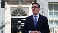 Andy Burnham i kostym och slips står framför en svart dörr på Downing Street i London. 