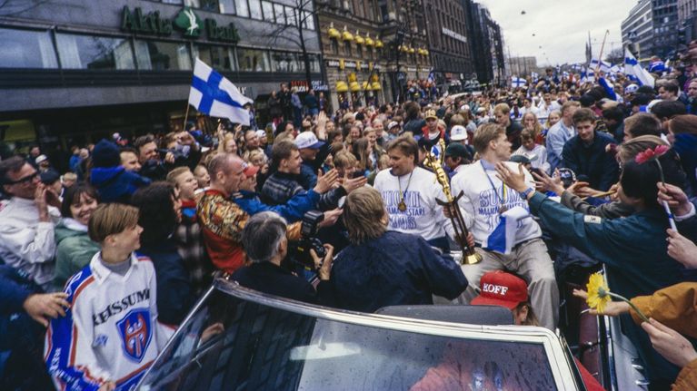 Ihmispaljous, jonka keskellä auto, jonka kyydissä Timo Jutila ja Saku Koivu. Jutila ja Koivu pitelevät MM-voittopokaalia, miesten kauloissa roikkuvat kultamitalit.