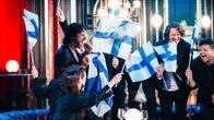 Joukko ihmisiä juhlii Suomen lippuja heiluttaen sisätiloissa.