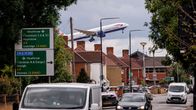 Lentokone laskeutumassa matalalla talojen yläpuolella, kadulla liikennettä ja tienviittoja Heathrow'n suuntaan.